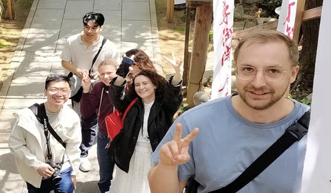 A group of people smile and make peace signs while posing for a selfie on outdoor stone steps.