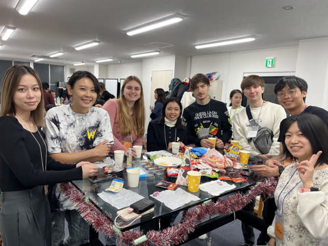 A group of people smiles for the camera while gathered around a glass table with snacks and decorations in an office.